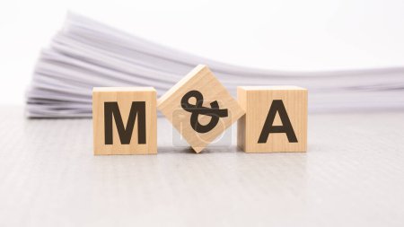 wooden cube with text M and A - acronym - Mergers and Acquisitions . wooden cubes are on the paper white background, business concept. front view.