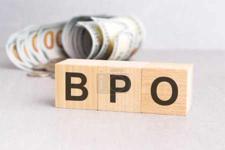 Holzblöcke mit den Buchstaben BPO auf der grauen Oberfläche des Tisches und Dollarscheine im Hintergrund