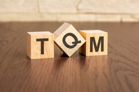 total quality management concept with symbols TQM on wooden cubes, dark wooden background