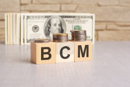 Palabra BCM sobre cubos de madera y billetes de dólar de fondo. Concepto de gestión de continuidad empresarial