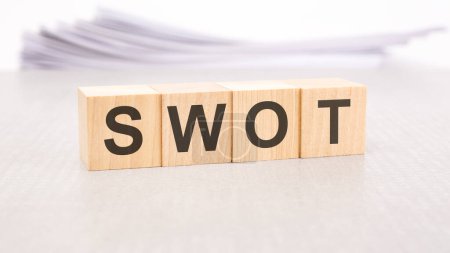 Foto de SWOT texto escrito en bloques de madera, pila de hojas blancas en el fondo - Imagen libre de derechos