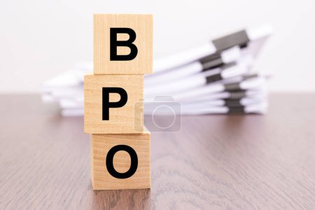Holzwürfel mit Buchstaben BPO in einer vertikalen Pyramide angeordnet, Stapel weißes Papier auf Hintergrund