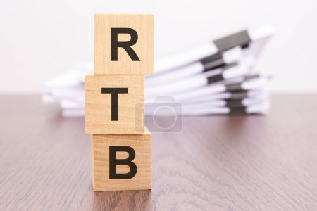 wooden cubes with letters RTB arranged in a vertical pyramid, stack white paper on background