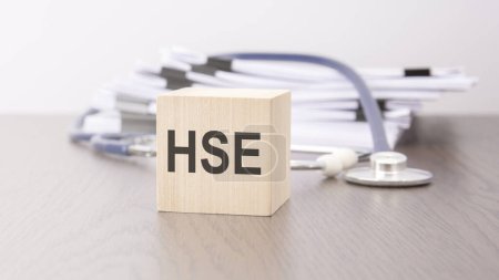 text HSE - 'HSE - Health and Safety Executive' is written on wooden block near a stethoscope on a grey background