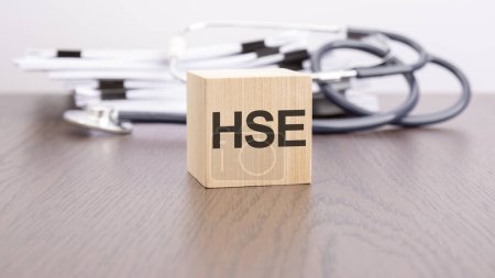 text HSE - HSE - Health and Safety Executive is written on wooden block near a stethoscope on a grey background