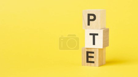 wooden cubes with text pte - short for pearson tests of english. yellow background