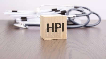 Text HPI - "HPI - Health Practice Index" steht auf einem Holzblock in der Nähe eines Stethoskops auf grauem Hintergrund.