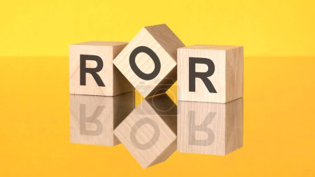 drei Holzwürfel mit dem Akronym ROR auf gelbem Hintergrund. Spiegelung eines Bildes auf einem Glasoberflächenkonzept