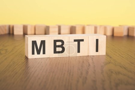 short word english letters with text - MBTI - on a small wooden blocks. brown background. selection focus.