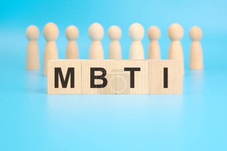 el término MBTI está inscrito en bloques de madera sobre un fondo azul brillante. la imagen tiene enfoque selectivo en cuatro bloques. figuras de madera de las personas en el fondo.