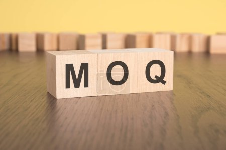 drei Holzwürfel auf braunem Hintergrund mit dem Text MOQ - eine Abkürzung für Minimum Order Quantity. Starkes Geschäftskonzept