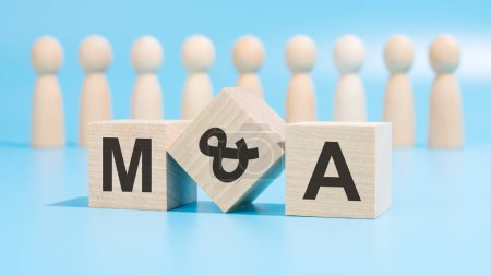 The photo showcases three small wooden blocks on a blue background, inscribed with letters M, A. Wooden figurines, blurred in the background, resemble a team.