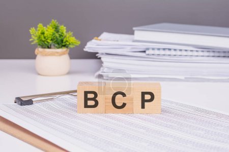 Photo for The cubes are used to form the word BCP. It is placed on a white paper document on the office desk. behind it is a stack of documents and a gray wall - Royalty Free Image