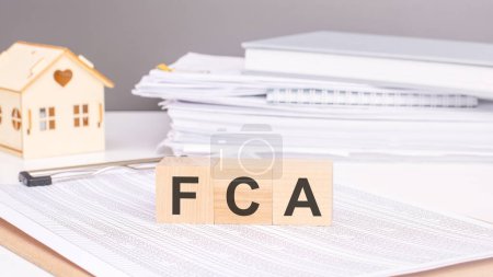 FCA-Text auf Holzklötzen auf Diagrammhintergrund mit einem kleinen hölzernen Modellhaus