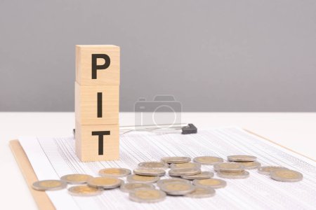 wooden blocks on a gray background with the text PIT - an abbreviation for Personal Income Tax. strong business concept