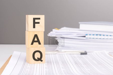 Photo for FAQ text on wood blocks on a document with tables on a stack of documents in the gray background - Royalty Free Image