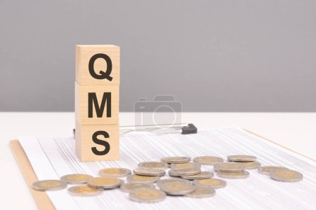 wooden blocks on a gray background with the text QMS - an abbreviation for Quality Management System. strong business concept