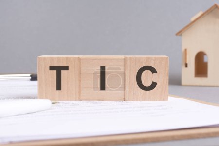 tic text made of wooden cubes on gray background with a small wooden model house. tic - short for tenancy in common