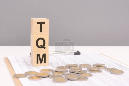 wooden blocks on a gray background with the text TQM - an abbreviation for Total Quality Management. strong business concept