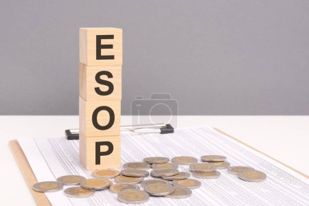 Palabra ESOP en bloques de madera con monedas apiladas en pilas crecientes. ESOP Employee Stock Ownership Plan representa un concepto potenciador en el que los empleados participan en el accionariado de la empresa.