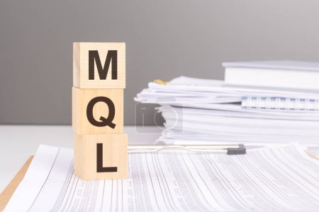 la disposición de cubos de madera ortografía 'MQL' sobre un telón de fondo de papeles de negocios simboliza un enfoque en la comunicación clara y el intercambio de información