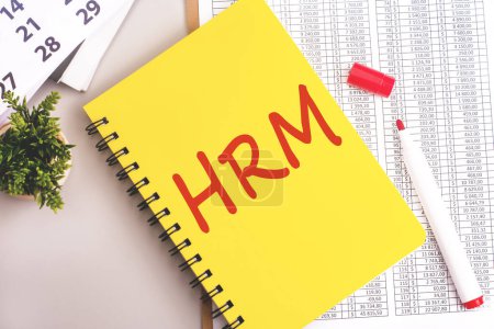 roter Marker, Finanzdokument, weißer Kalender und gelbes Notizbuch mit HRM-Zeichen auf grauem Hintergrund