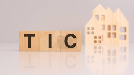TIC text made of wooden cubes on background with a small model houses. image is reflected on the surface. the image symbolizes the importance of contractual commitments and business integrity