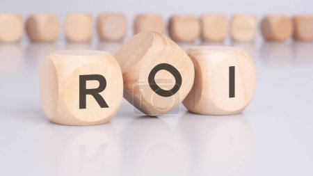 three wooden cubes with the letters ROI on the bright surface of a gray table. the inscription on the cubes is reflected from the surface of the table. ROI - short for return on investment