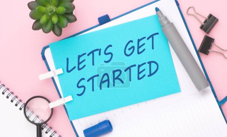 The text 'LET'S GET STARTED' on a blue sheet against a pink background evokes the concept of initiation, beginning, and taking action towards a goal or project.