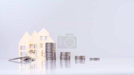 Stapel von Münzen und Schlüssel auf grauem Hintergrund mit Modellhaus mit Spiegelung