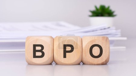 wooden cubes spelling out 'BPO' on the office table, with a white paper document and green plant in the background, conveys a business concept