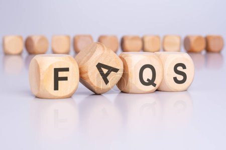 Photo for Four wooden blocks with the letters FAQS standing at an angle to the viewer on a light gray table and reflecting of the surface. there are many cubes with no inscription in the background - Royalty Free Image