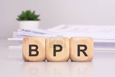 Holzwürfel mit der Aufschrift "BPR" auf dem Bürotisch, im Hintergrund ein Dokument aus weißem Papier, bpr - Abkürzung für Business Process Reengineering