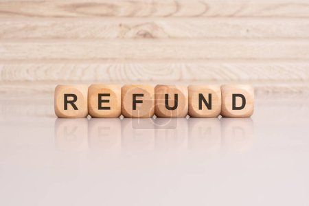 wooden cubes displaying the word 'Refund' arranged on a glossy gray surface, with a reflection and wooden background