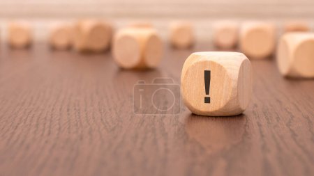 in the foreground is one wooden cube with a exclamation point and a reflection from the table surface. in the background is a row of wooden blocks (out of focus).