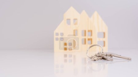 Hausschlüssel in Großaufnahme, mit unscharfen Hausmodellen im Hintergrund und selektivem Fokus. vermittelt ein Immobilienkonzept