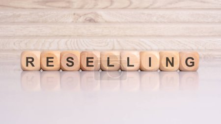 Wooden blocks spelling 'RESELLING' against a gray backdrop suggest a profitable commerce practice. Resale involves redistributing acquired goods for profit.