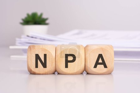 Holzwürfel mit der Aufschrift "NPA" auf dem Bürotisch, auf dem Hintergrund ein Dokument aus weißem Papier, NPA - kurz für Non Performing Assets