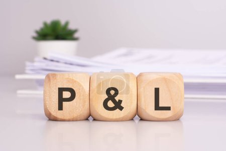 wooden cubes spelling out 'P and L' on the office table, with a white paper document on the background, P and L - short for profit and loss