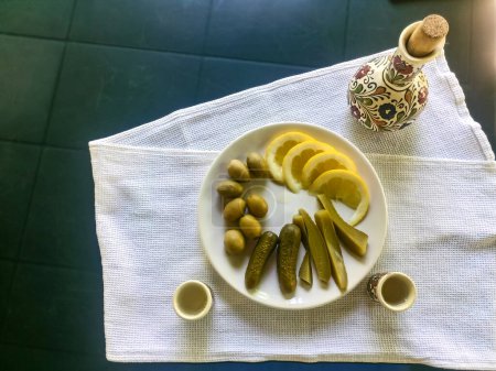 small jug for strong alcohol prepared in the country with olives, pickled cucumbers and lemon, on a white towel. Traditional holiday meal concept in the country. old country traditions