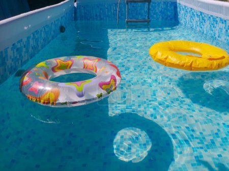 Téléchargez les photos : Flotteur de piscine jaune, anneau de piscine dans une piscine bleue rafraîchissante et fraîche. Remplir la piscine d'eau Le début de la saison balnéaire dans la piscine - en image libre de droit
