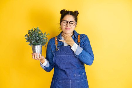 Photo for Young caucasian gardener woman holding a plant isolated on yellow background touching painful neck, sore throat for flu, clod and infection - Royalty Free Image