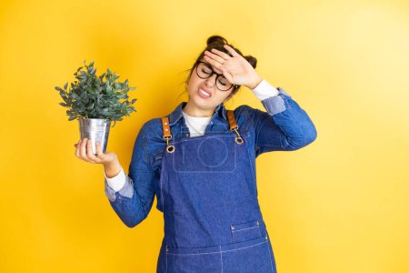 Photo for Young caucasian gardener woman holding a plant isolated on yellow background Touching forehead for illness and fever, flu and cold, virus sick - Royalty Free Image