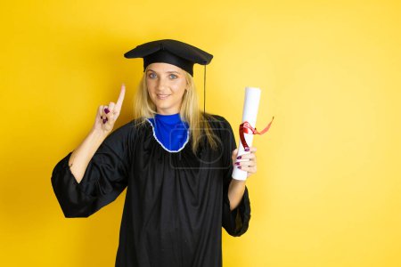 Beautiful blonde young woman wearing graduation cap and ceremony robe surprised and thinking with her finger on her head that she has an idea.