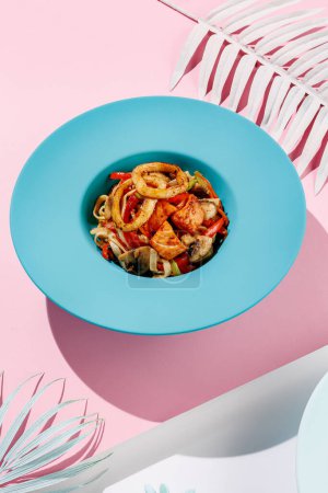 Foto de Udon with calamary and vegetables, seafood on blue pastel color plate at white background with sunlight and shadows, minimalism, squid. - Imagen libre de derechos