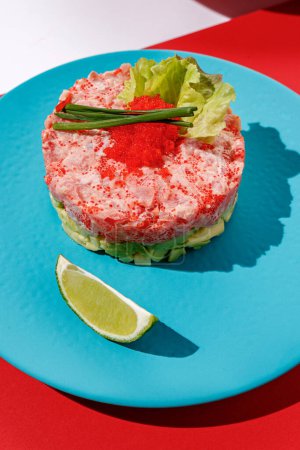 Téléchargez les photos : Tartar with tuna and caviar with lime at blue pastel color plate at blue at red background with sunlight and shadows, minimalism,top view. - en image libre de droit