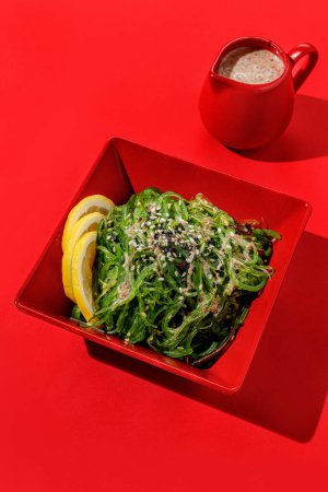 Téléchargez les photos : Salade d'algues vertes comestibles avec sauce aux noix en boule de couleur rouge à fond rouge avec lumière du soleil et ombres, minimalisme. - en image libre de droit
