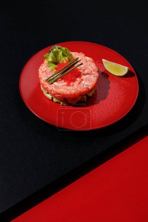 Téléchargez les photos : Tartare au saumon et caviar à la chaux à la plaque de couleur rouge à fond noir et rouge avec lumière du soleil et ombres, minimalisme, vue de dessus. - en image libre de droit