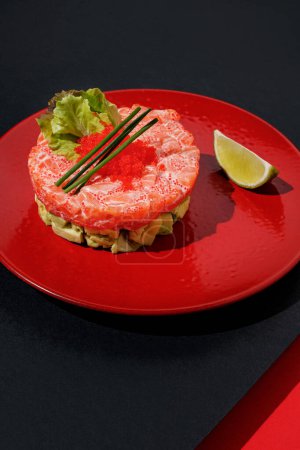 Téléchargez les photos : Tartar with salmon and caviar with lime at red color plate at black and red background with sunlight and shadows, minimalism,top view - en image libre de droit