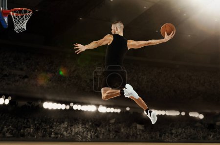 Photo for Slam dunk. Young professional basketball player playing basketball at basketball court with people fans. Photoreal 3d render of sport arena. Concept of sport, energy, power, motion. - Royalty Free Image